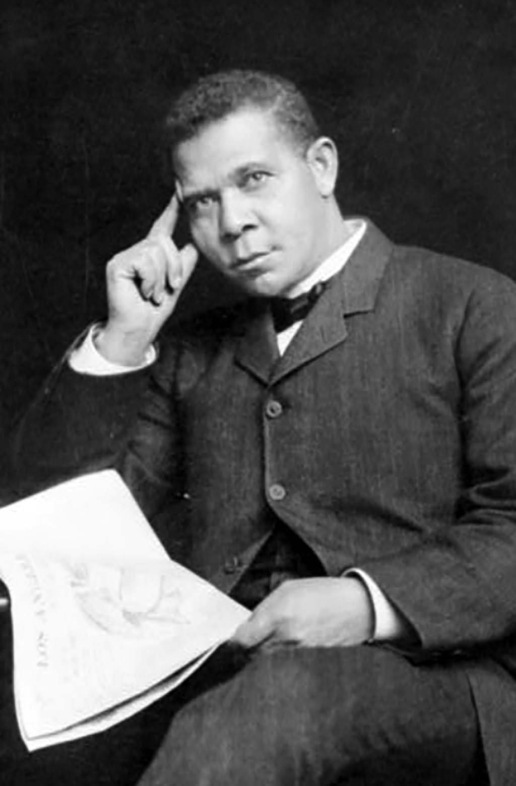 Booker T. Washington, three-quarter length portrait, seated, facing slightly left, holding newspaper