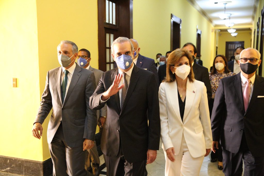 Abinader waving while walking down a hallway and wearing a face mask